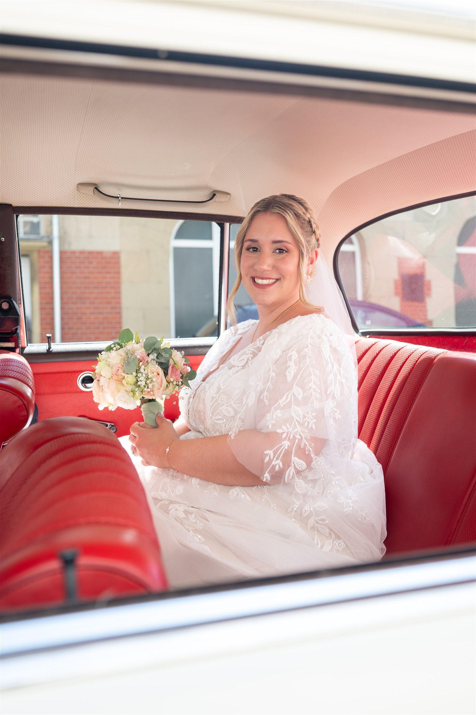 Jule sitzt mit ihrem Brautstrauß im historischen Hochzeitsauto