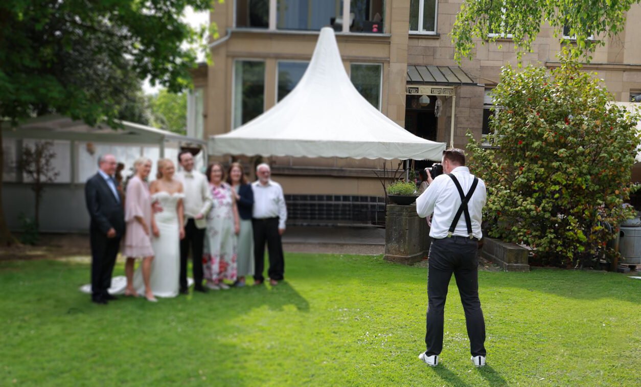 Michael fotografiert ein Brautpaar mit seiner Familie im Garten.
